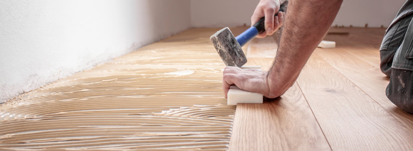 Handwerker klopft Holzdielen mit Hammer zur Verlegung zusammen